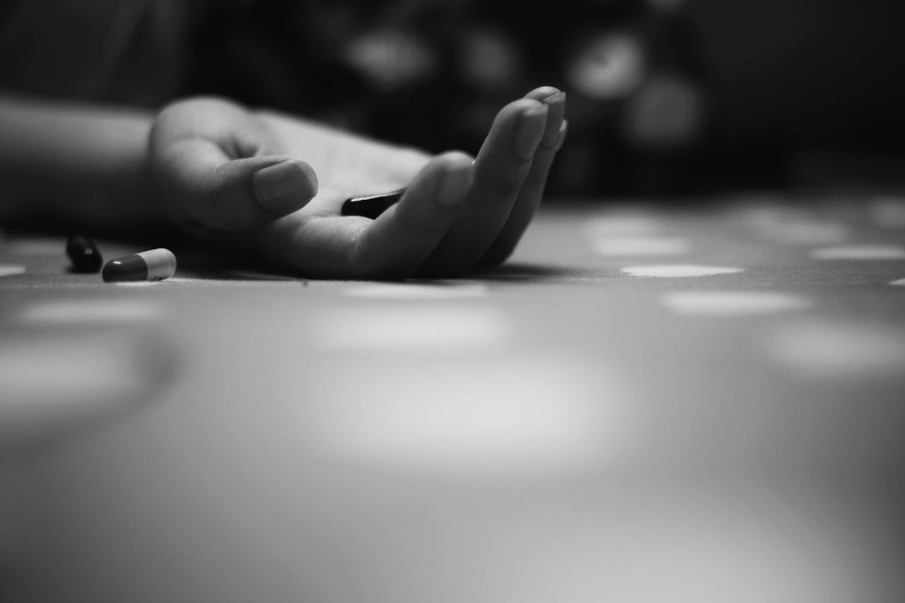 Close-up black and white image of a hand with pills on a textured surface. Moody atmosphere.